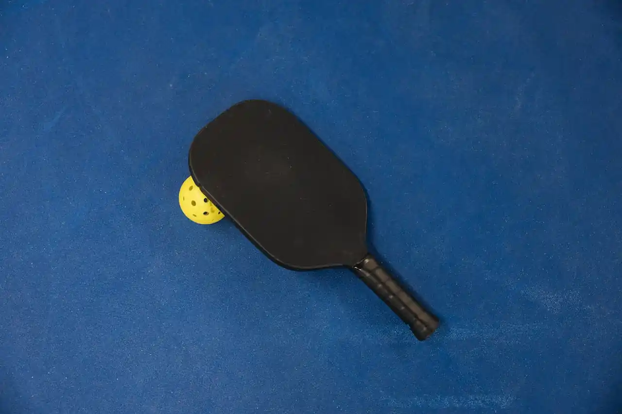 A black pickleball paddle resting on a court surface, representing the gear needed for park play