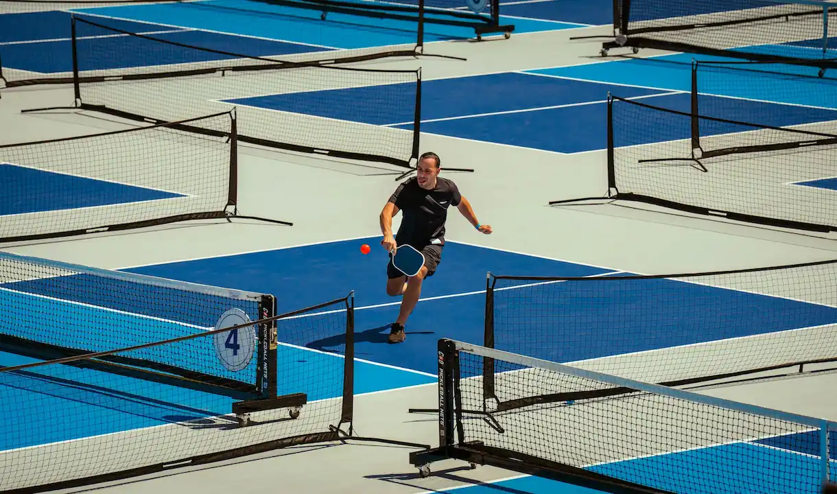 A competitive pickleball player executing a backhand drive at an indoor facility in Fort Worth