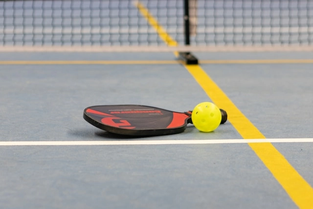 A pickleball paddle and ball resting on the floor of an indoor facility in Miami