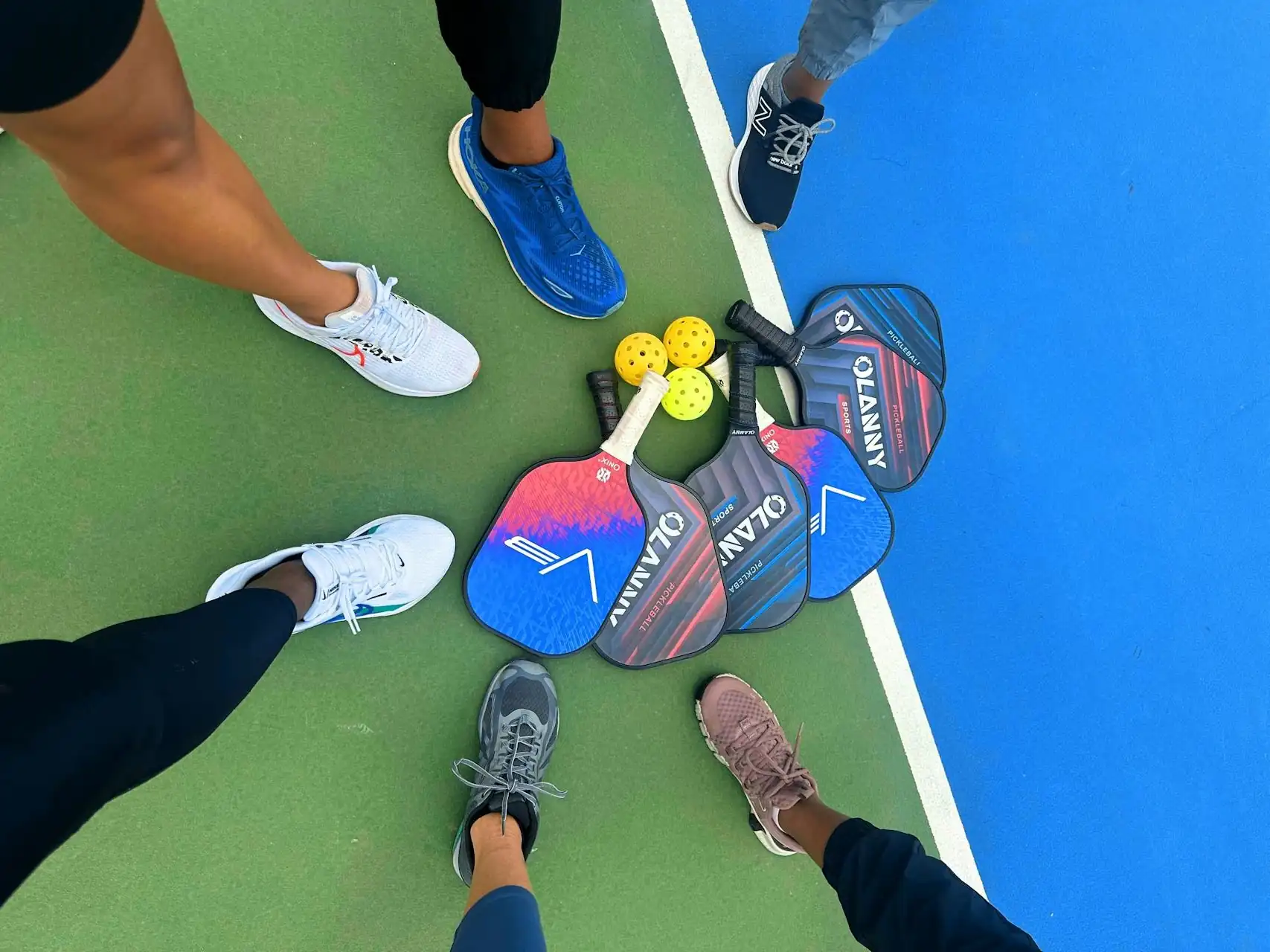 A group of pickleball players gathered around a paddle stack at a public park, illustrating the social 'open play' culture