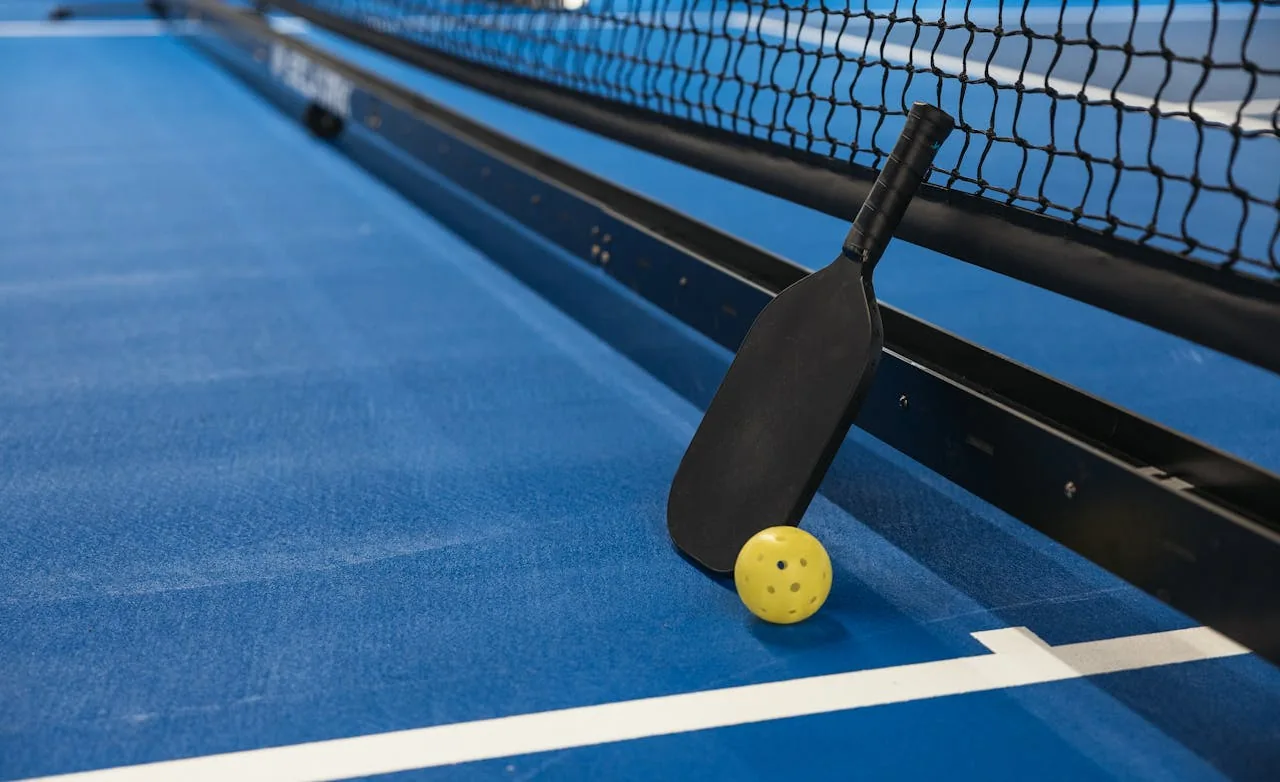 Close up of a pickleball paddle and ball on an indoor court surface
