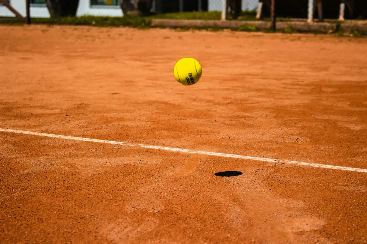 A tennis ball landing on the soft Har-Tru clay surface at Sterling Oaks, kicking up a small cloud of green dust