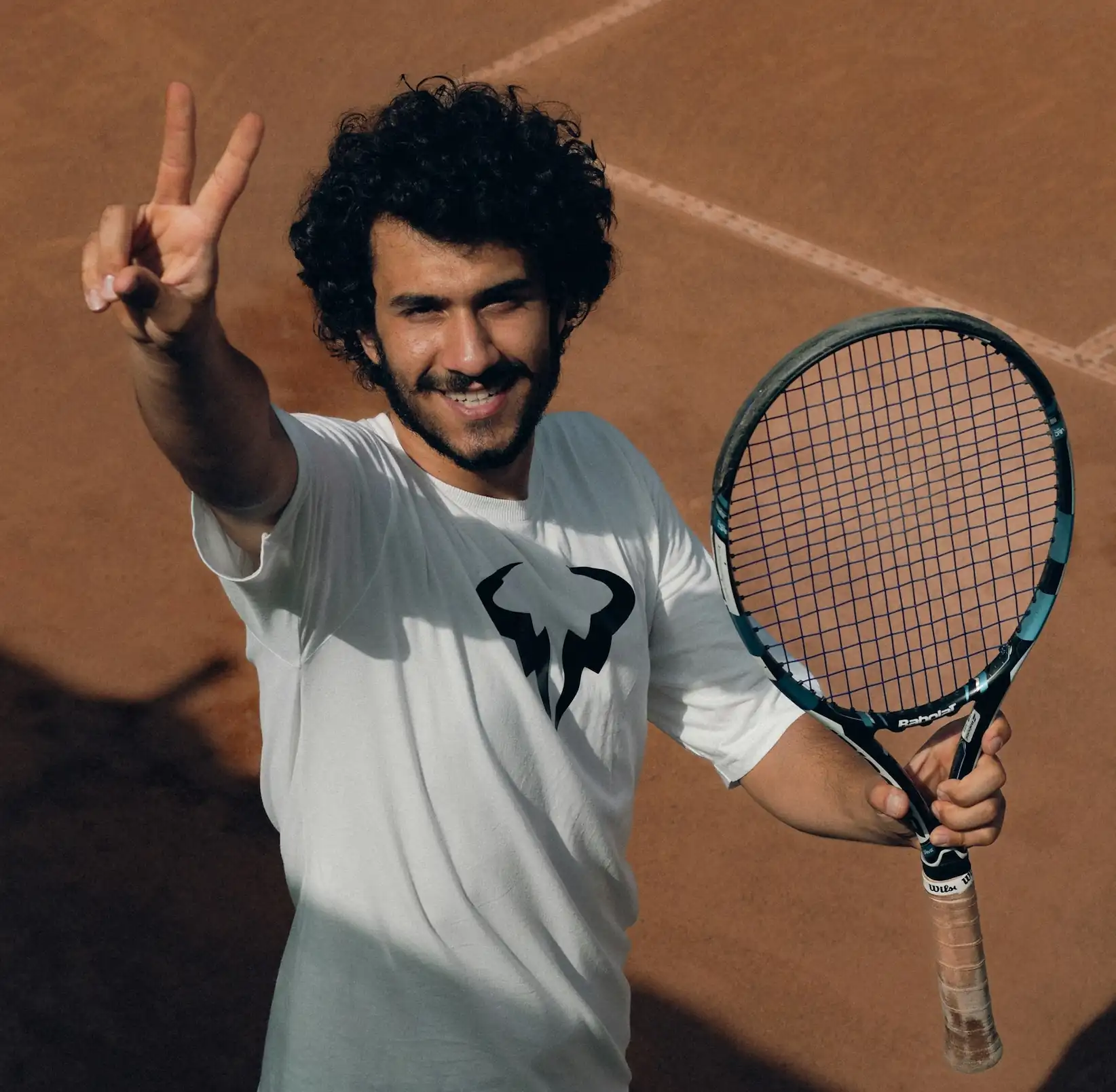 Male private tennis instructor holding a peace sign and tennis racquet, available for mobile lessons in Atlanta, GA.