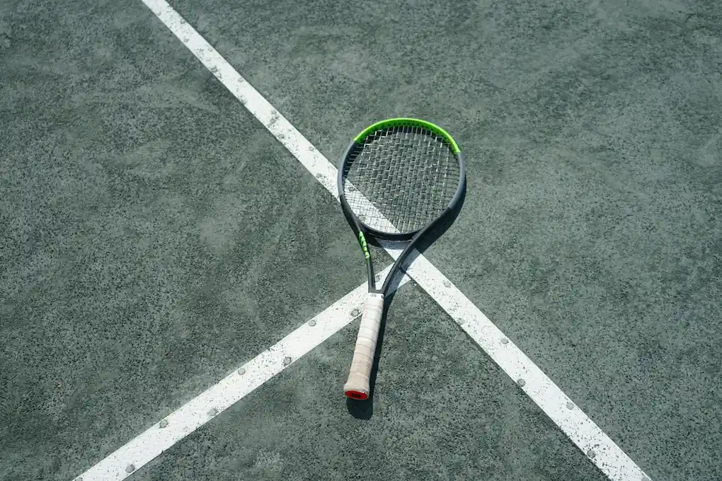 A tennis racquet resting on the floor of a professionally lit indoor tennis facility