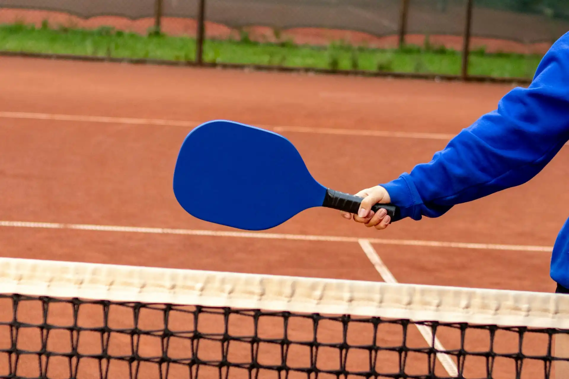 A close-up of a pickleball paddle over a portable net, which is required at most Frisco public parks