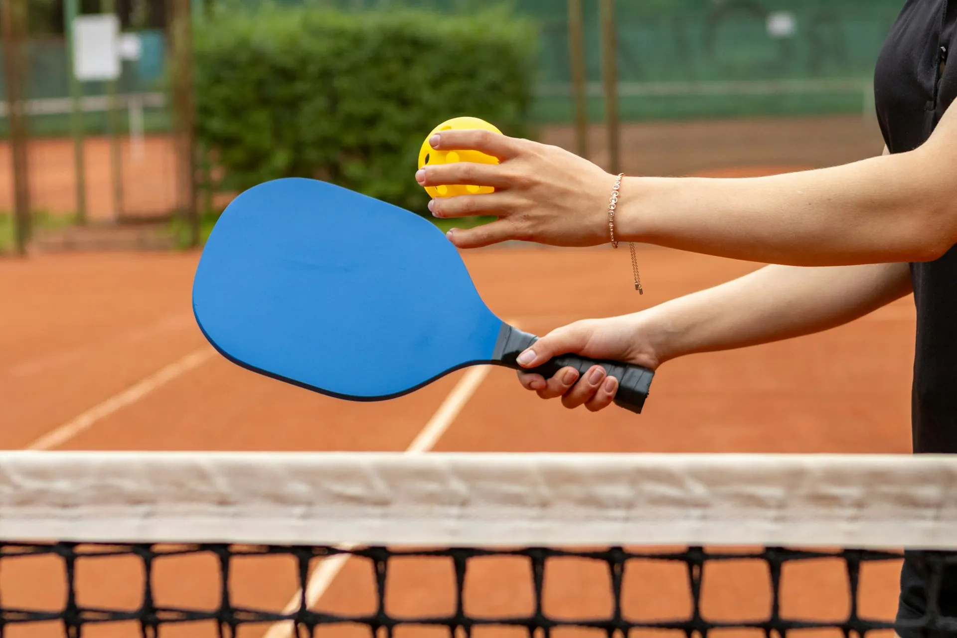 A woman holding a pickleball and paddle in front of a net at a Miami court, ready to play