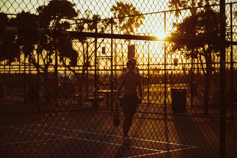 Man playing pickleball with a vivid coastal sunset behind him