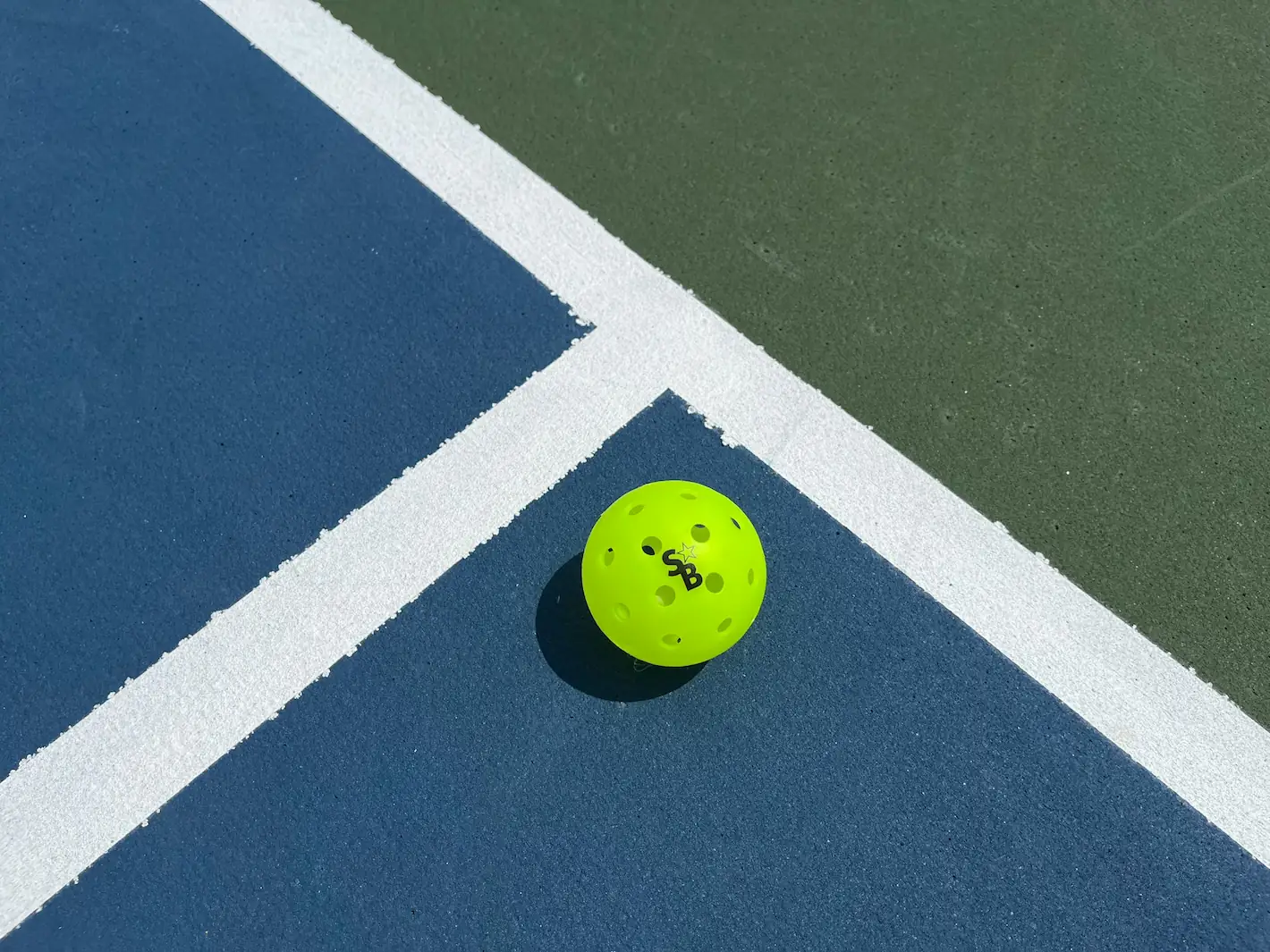 A pickleball resting on an outdoor pickleball court